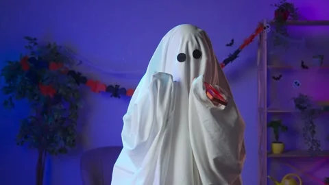 Funny halloween ghost in white sheet with black eyes in dark room talking on Stock Footage 285742146