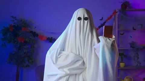 Funny halloween ghost in white sheet with black eyes in dark room talking on Stock Footage 285742298