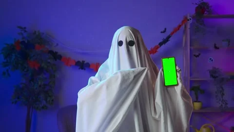 Funny halloween ghost in white sheet with black eyes in dark room holding Stock Footage 285742780