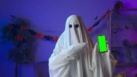 Funny halloween ghost in white sheet with black eyes in dark room holding Stock Footage 285742829