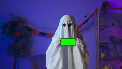 Funny halloween ghost in white sheet with black eyes in dark room holding Stock Footage 285742934