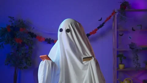 Funny halloween ghost in white sheet with black eyes in dark room typing credit Stock-Footage 285743015
