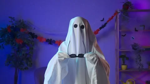 Funny halloween ghost in white sheet with black eyes in dark room looks at Stock Footage 285743064