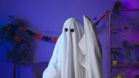 Funny halloween ghost in white sheet with black eyes in dark room confused Stock Footage 285743577
