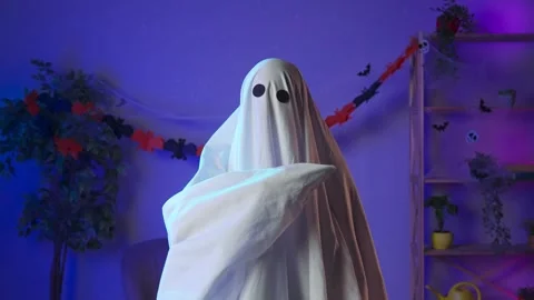 Funny halloween ghost in white sheet with black eyes in dark room looks at Stock Footage 285743774