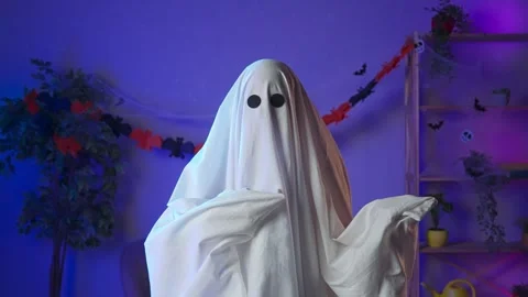 Funny halloween ghost in white sheet with black eyes in dark room looks at Stock Footage 285743930