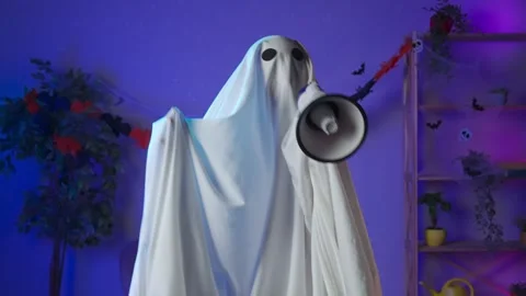 Funny halloween ghost in white sheet with black eyes in dark room speaking Stock Footage 285744326