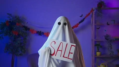 Funny halloween ghost in white sheet with black eyes in dark room holding Stock Footage 285744738