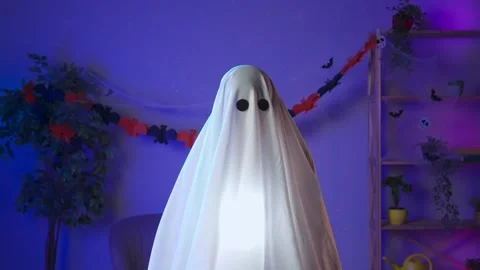 Funny halloween ghost in white sheet with black eyes in dark room and lighted up Stock Footage 285745144