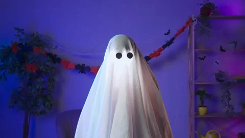 Funny halloween ghost in white sheet with black eyes in dark room and lighted up Stock Footage 285745167