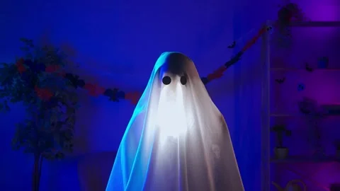 Funny halloween ghost in white sheet with black eyes in dark room and lighted up Stock Footage 285745274