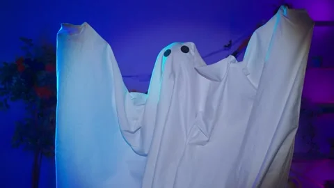 Funny halloween ghost in white sheet with black eyes in dark room and lighted up Stock Footage 285745541
