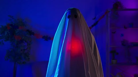 Funny halloween ghost in white sheet with black eyes in dark room and lighted up Stock Footage 285745628