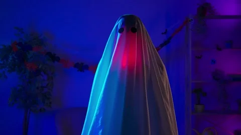 Funny halloween ghost in white sheet with black eyes in dark room and lighted up Stock Footage 285745661