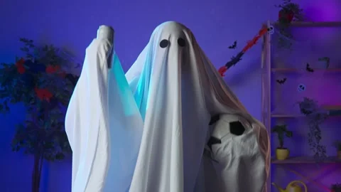 Funny halloween ghost in white sheet with black eyes in dark room holding Stock Footage 285745971