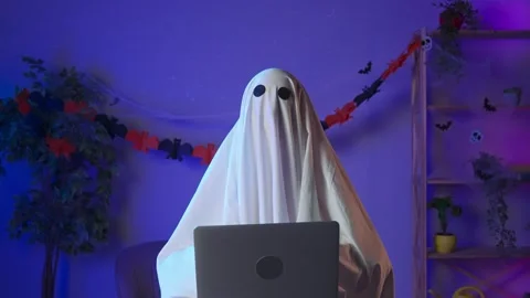Funny halloween ghost in white sheet with black eyes in dark room working on Stock Footage 285746052