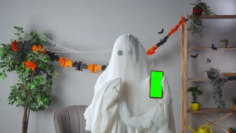 Funny halloween ghost in white sheet with black eyes in bright room holding Stock Footage 285746353