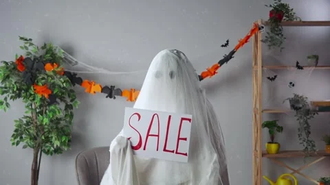 Funny halloween ghost in white sheet with black eyes in bright room holding Stock Footage 285746526