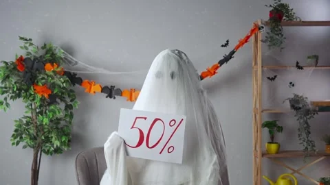 Funny halloween ghost in white sheet with black eyes in bright room holding Stock Footage 285746534