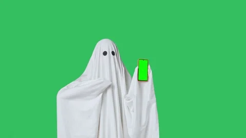 Funny halloween ghost in white sheet pointing shows thumb up at smartphone Stock Footage 285747340