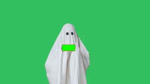 Funny halloween ghost in white sheet pointing shows thumb up at smartphone Stock Footage 285747425