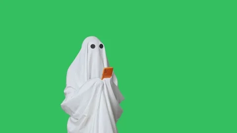 Funny halloween ghost in white sheet texting on smartphone scrolling social Stock Footage 285748793