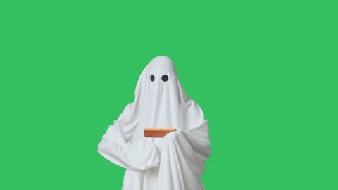 Funny halloween ghost in white sheet plays video game on smartphone, lost sad Stock Footage 285749030