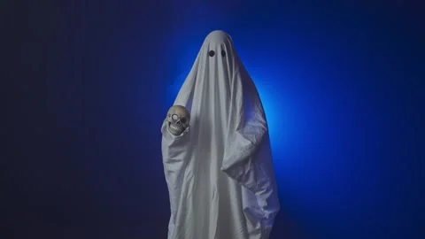 Funny halloween ghost in white sheet holding skull head looking scary at camera Stock Footage 285752523