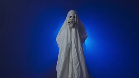 Funny halloween ghost in white sheet holding skull head looking scary at camera Stock Footage 285752627