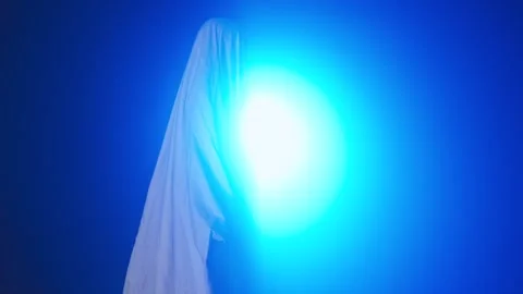 Funny halloween ghost in white sheet silhouette walking past bright blue Stock Footage 285753841