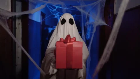 Funny halloween ghost in white sheet giving gift box with red bow while standing Stock Footage 313555101