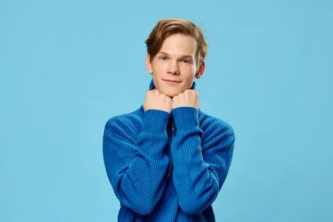 A funny handsome red-haired guy in a blue jacket with a zipper stands on a light Stock Photos