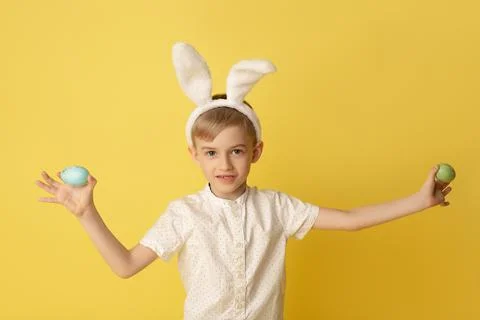 Funny happy child boy with easter eggs and bunny ears on yellow background Stock Photos