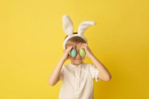Funny happy child boy with easter eggs and bunny ears on yellow background Stock Photos