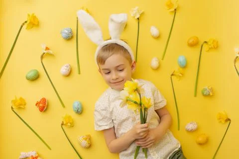 Funny happy child boy with easter eggs and spring flowers on yellow Stock Photos