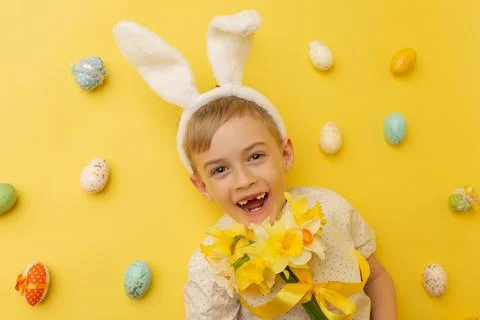 Funny happy child boy with easter eggs and spring flowers on yellow Stock Photos