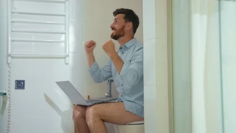 Funny happy man workaholic is working in toilet on computer smiling reading good Stock Footage 132541175