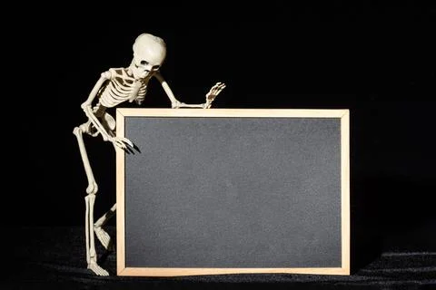 Funny human skeleton standing next to a black empty flipchart on a black back Stock Photos