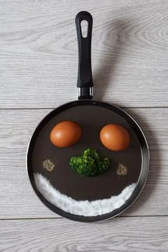 Funny image of a face made of eggs, broccoli in a frying pan. Stock Photos