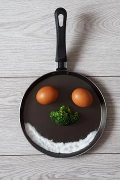 Funny image of a face made of eggs, salt, broccoli in a frying pan. Stock Photos