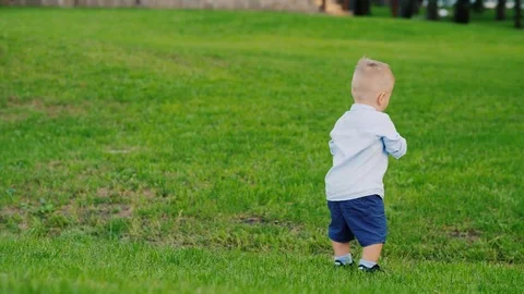 Funny kid 1 year is drinking water from a bottle. It stands on a green lawn Stock Footage 80017478