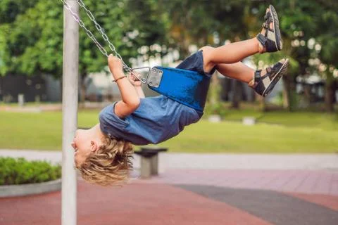 Funny kid boy having fun with chain swing on outdoor playground. child swinging Stock Photos