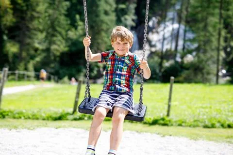 Funny kid boy having fun with chain swing on outdoor playground during rain Stock Photos