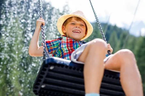 Funny kid boy having fun with chain swing on outdoor playground while being wet Stock Photos