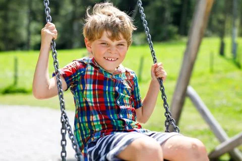 Funny kid boy having fun with chain swing on outdoor playground while being wet Stock Photos