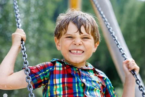 Funny kid boy having fun with chain swing on outdoor playground while being wet Stock Photos