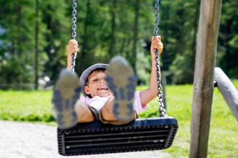 Funny kid boy having fun with chain swing on outdoor playground while being wet Stock Photos
