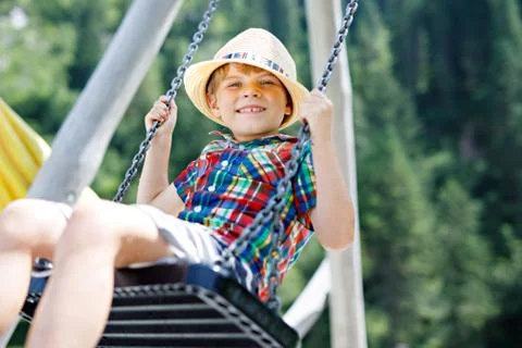 Funny kid boy having fun with chain swing on outdoor playground while being wet Stock Photos