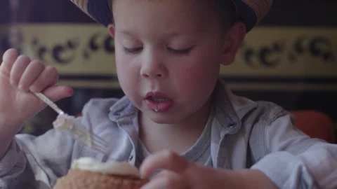 Funny kid in hat enthusiasm concentration eats dessert cafe. 5 year old boy eat Stock-Footage 247220103