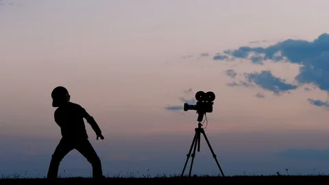 Funny kid playing role in front of photo video camera outdoor at sunset Stock Footage 98280039